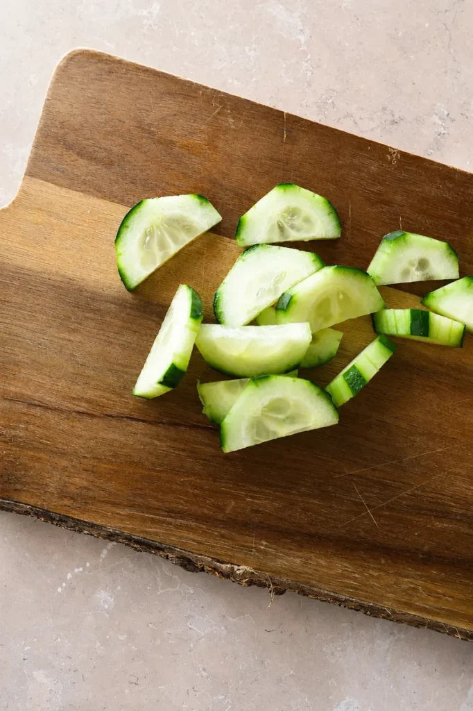 Sliced cucumber on a wooden cutting board for cantaloupe cucumber salad
