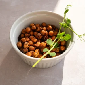 crispy chickpeas in a white bowl with fresh microgreens, photographed in natural light with soft shadows on a neutral stone background.