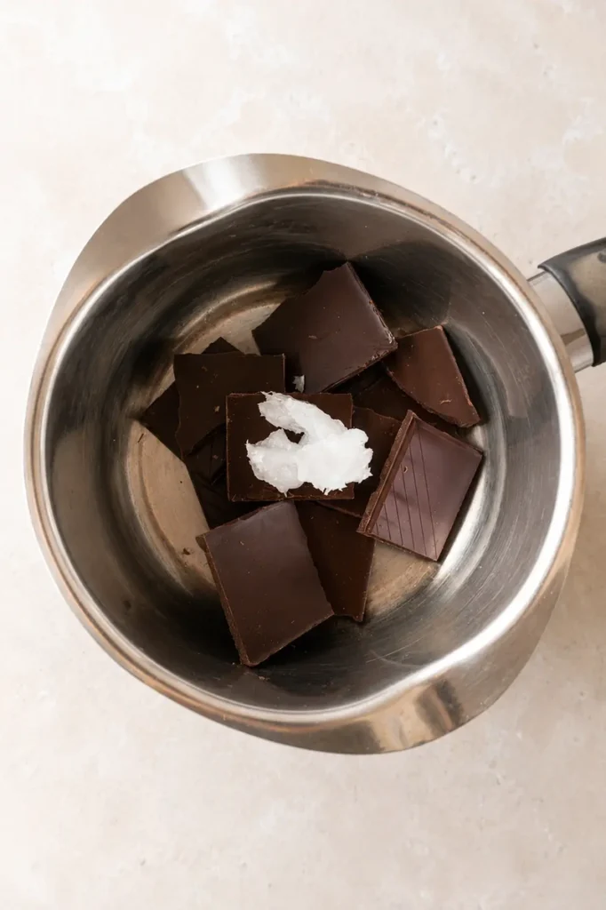 Easy Vegan Twix Bars with Dates chocolate pieces and coconut oil in a saucepan, ready to melt for the coating.