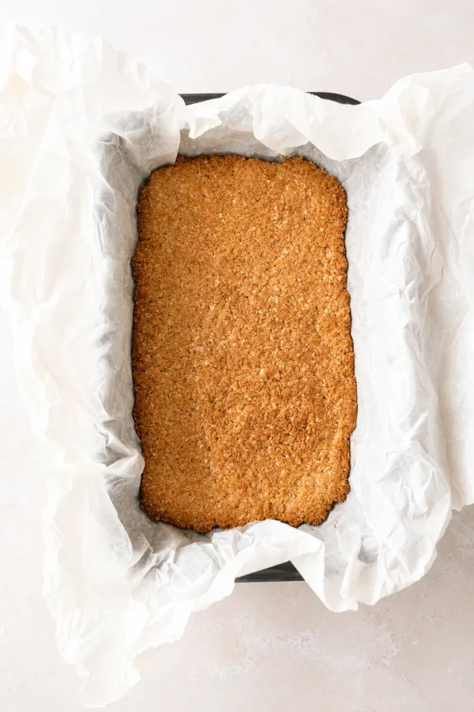 Easy Vegan Twix Bars with Dates baked oat base in a parchment-lined pan, golden and ready for the caramel layer.