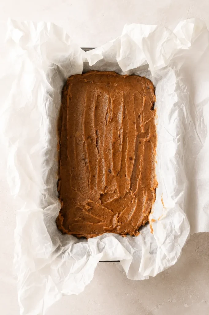 Easy Vegan Twix Bars with Dates date caramel layer smoothed over the oat base in a parchment-lined pan.