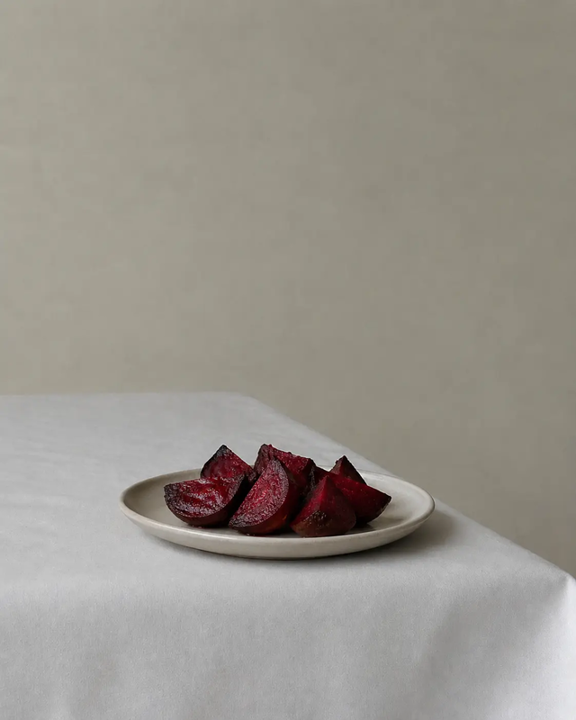 Cooked beetroot wedges served on a white plate, with caramelized edges and deep red color on a light fabric table.