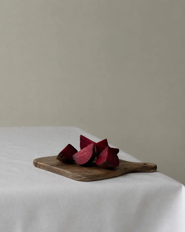 Beetroot wedges on a wooden cutting board, displayed on a light fabric table in a minimal editorial food composition.