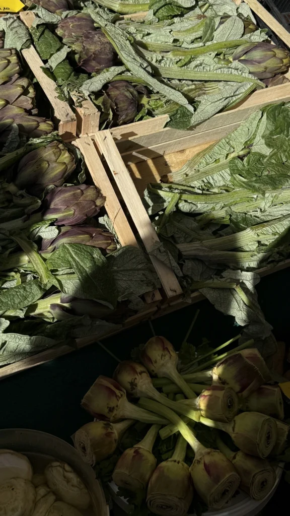 Is vegan diet healthy with fresh artichokes displayed in wooden market crates, surrounded by leafy greens and natural sunlight.