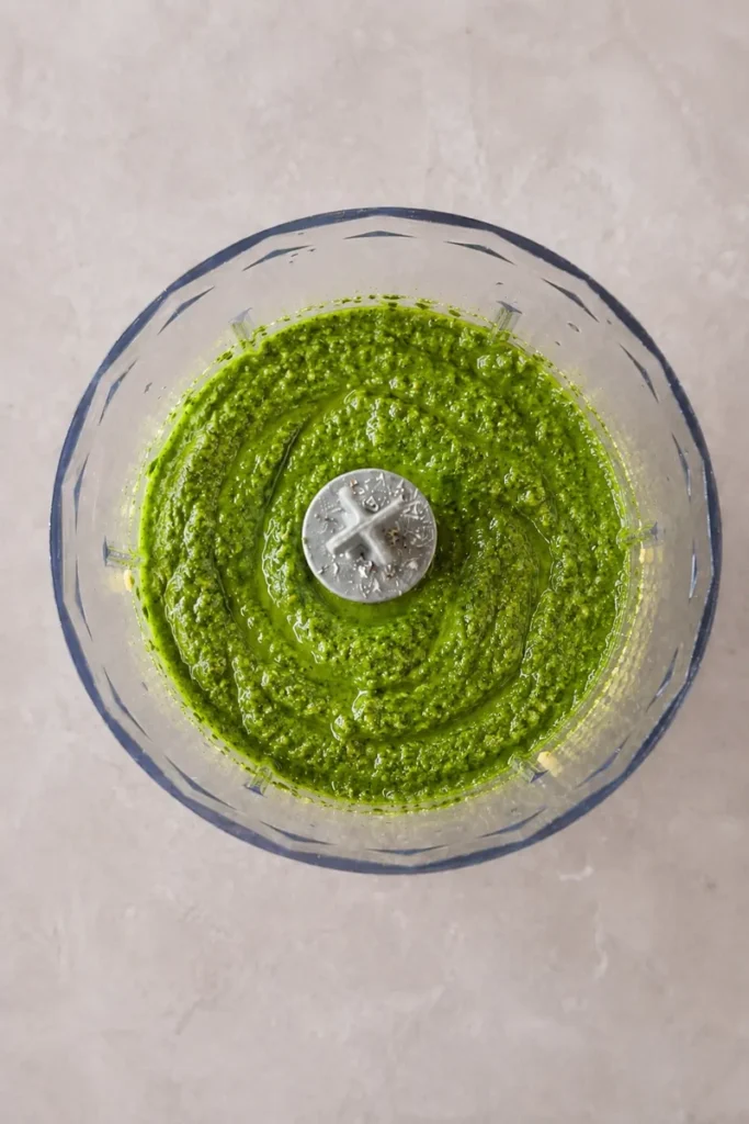 Vegan pesto pasta sauce blended into a bright green homemade pesto in a food processor.