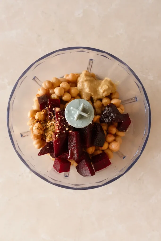 Pink hummus ingredients in a blender bowl, with chickpeas, beetroot, tahini, and seasonings ready to be blended.