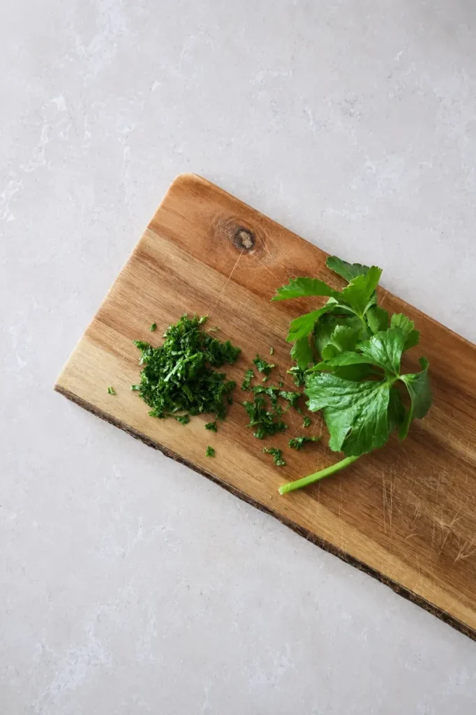 Potato puree chopped parsley on a wooden cutting board, with fresh parsley leaves beside it in an overhead preparation shot.
