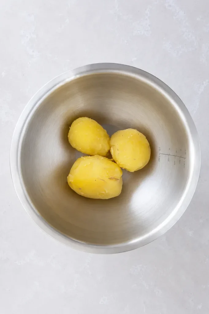 Potato puree boiled potatoes in a stainless steel bowl, shown peeled and ready to be seasoned and mashed.