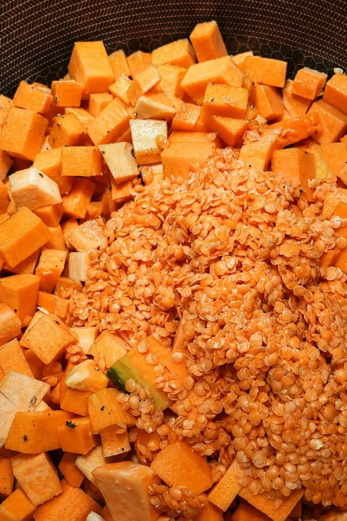 Pumpkin and red lentil soup ingredients cooking with pumpkin cubes and red lentils in a pot.
