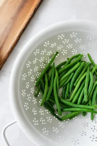 Roasted green beans recipe preparation with fresh green beans rinsed in a colander before trimming and seasoning.