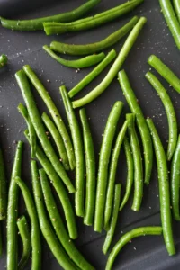 Close-up of roasted green beans with golden garlic pieces and a lightly crisp texture, served as a simple vegan side dish.