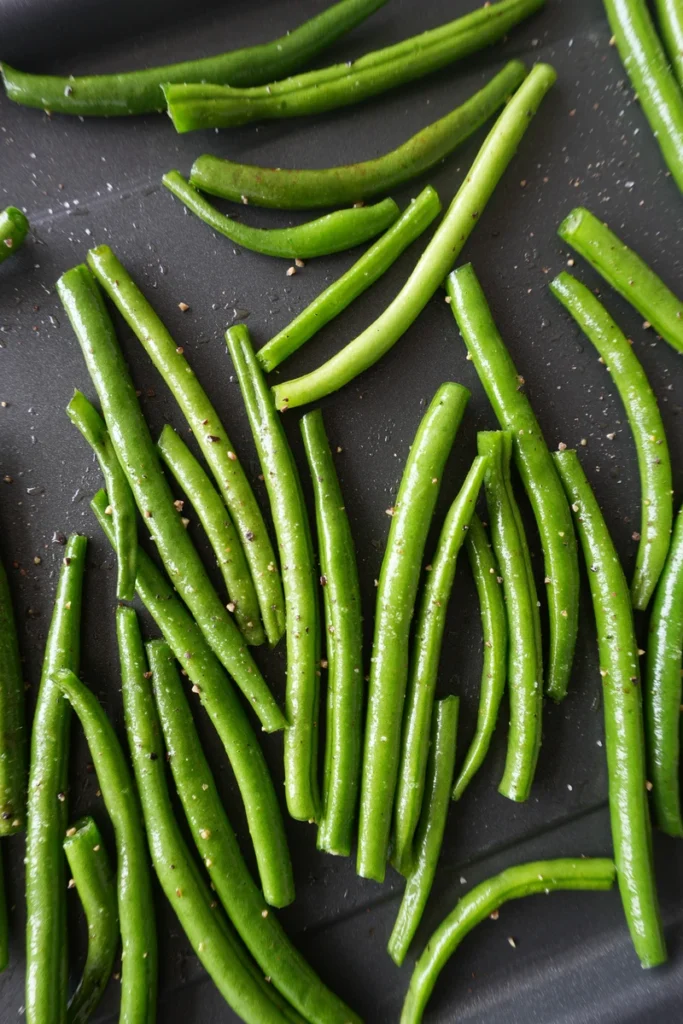 Close-up of roasted green beans with golden garlic pieces and a lightly crisp texture, served as a simple vegan side dish.