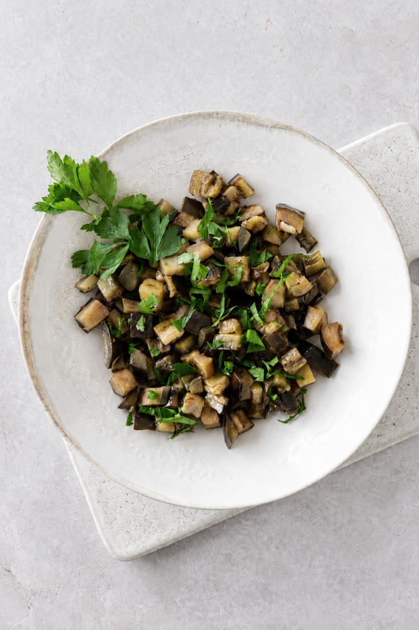 Sauteed eggplants with garlic and herbs served in a ceramic bowl with fresh parsley on top.