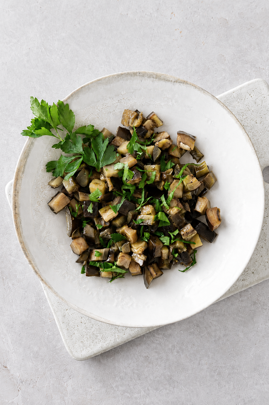 Sauteed eggplants with garlic and herbs served in a ceramic bowl with fresh parsley on top.