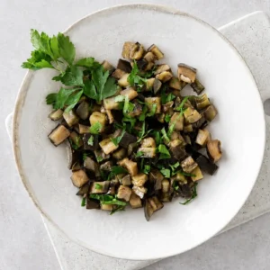 Sauteed eggplants with garlic and herbs served in a ceramic bowl with fresh parsley on top.