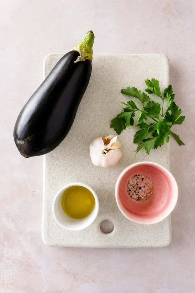 Sauteed eggplants with garlic and herbs ingredients with eggplant, parsley, garlic, olive oil, salt and pepper on a light board.
