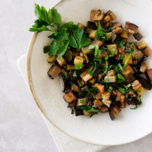 Sauteed eggplants with garlic and herbs close-up served in a neutral ceramic bowl with chopped parsley.