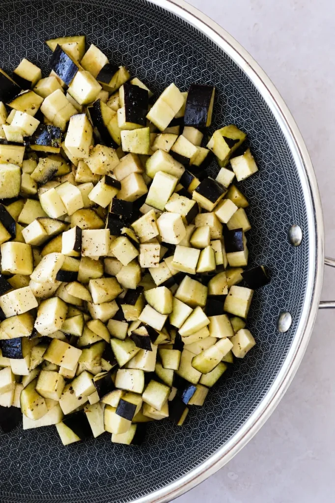 Sauteed eggplants with garlic and herbs cooking in a pan with diced eggplant, olive oil, salt and pepper.