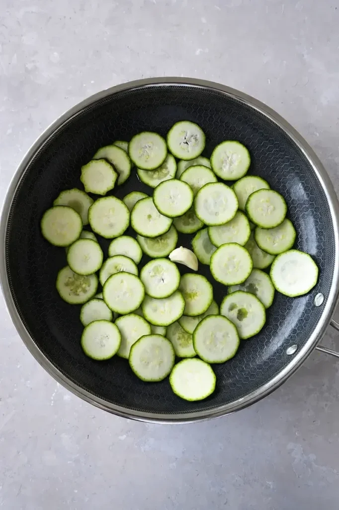 Zucchini recipe step with sautéed zucchini slices and garlic in a nonstick pan, photographed from above.