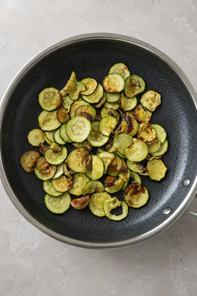 Zucchini recipe step with sautéed zucchini slices and garlic in a nonstick pan, cooked, photographed from above.