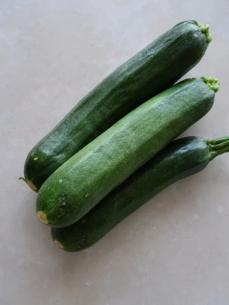 Zucchini close-up with three fresh whole zucchini on a light stone background, photographed in soft natural light.
