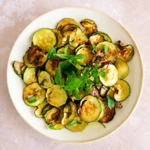 Overhead view of sautéed zucchini with lemon and fresh mint served on a white ceramic plate.