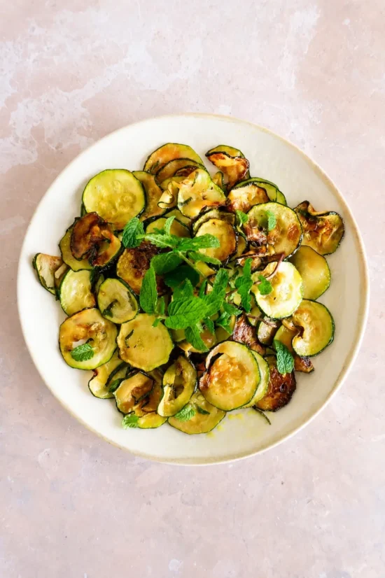 Overhead view of sautéed zucchini with lemon and fresh mint served on a white ceramic plate.