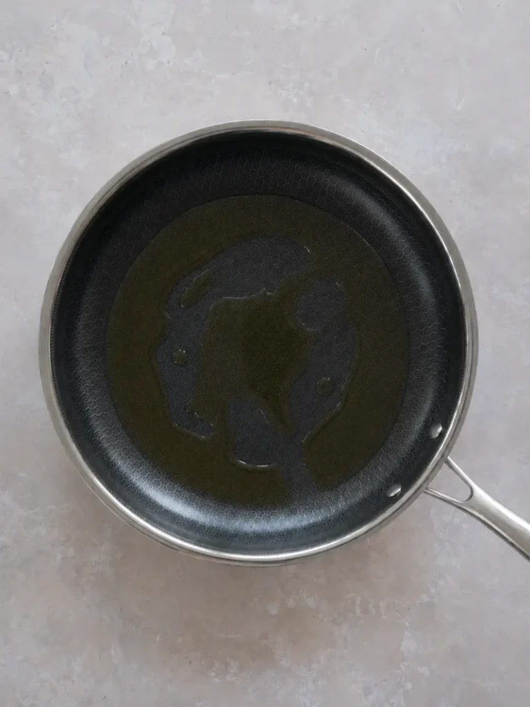 Zucchini recipe step with olive oil spread across a nonstick pan, ready for cooking the zucchini slices.