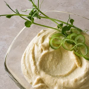 Vegan aioli served in a glass dish with a creamy texture, topped with fresh pea shoots and sliced spring onion.