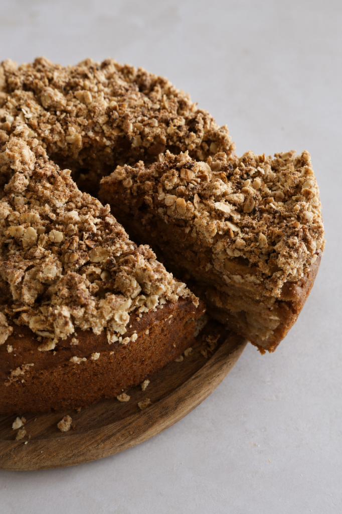 Vegan apple cake with a crunchy oat crumble topping, served on a wooden board with one slice cut out.