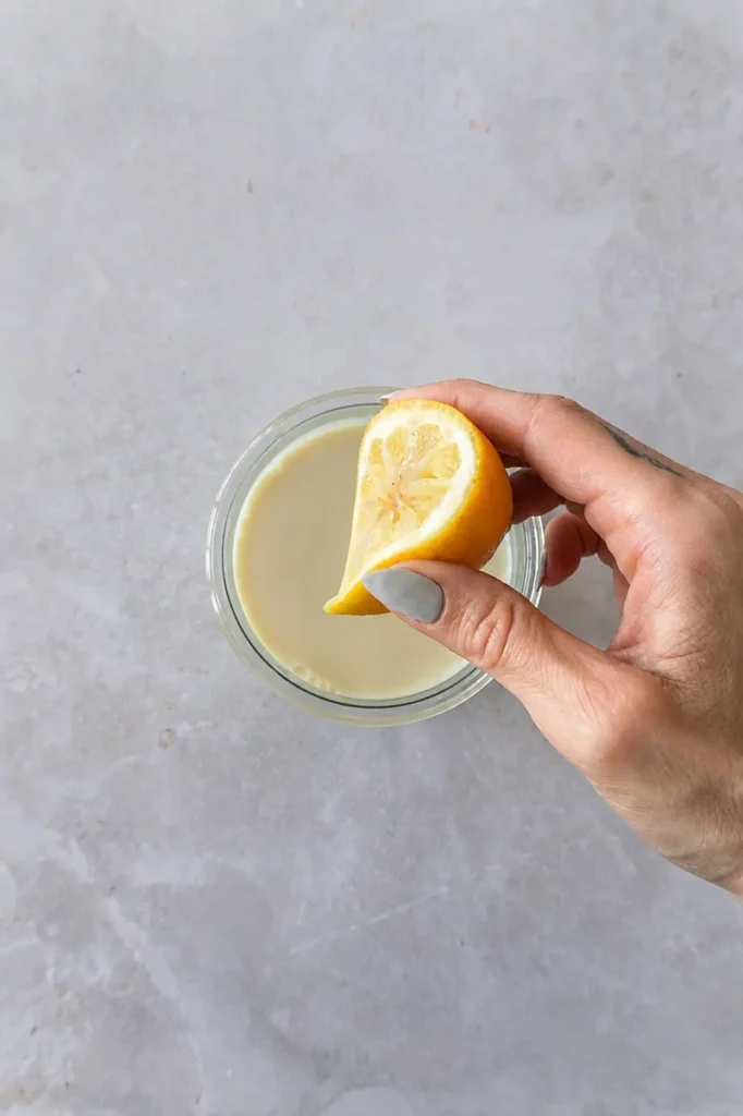 Lemon wedge held above a jar of plant-based milk for a vegan apple cake recipe.