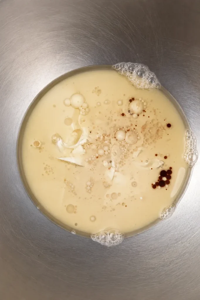 Vegan apple cake wet ingredients with soy milk, oil, yogurt, lemon juice, and vanilla mixed in a stainless steel bowl.