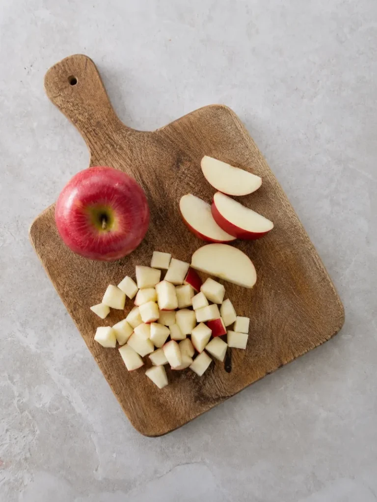Vegan apple cake recipe step showing a red apple cut on a long wooden board during the preparation process