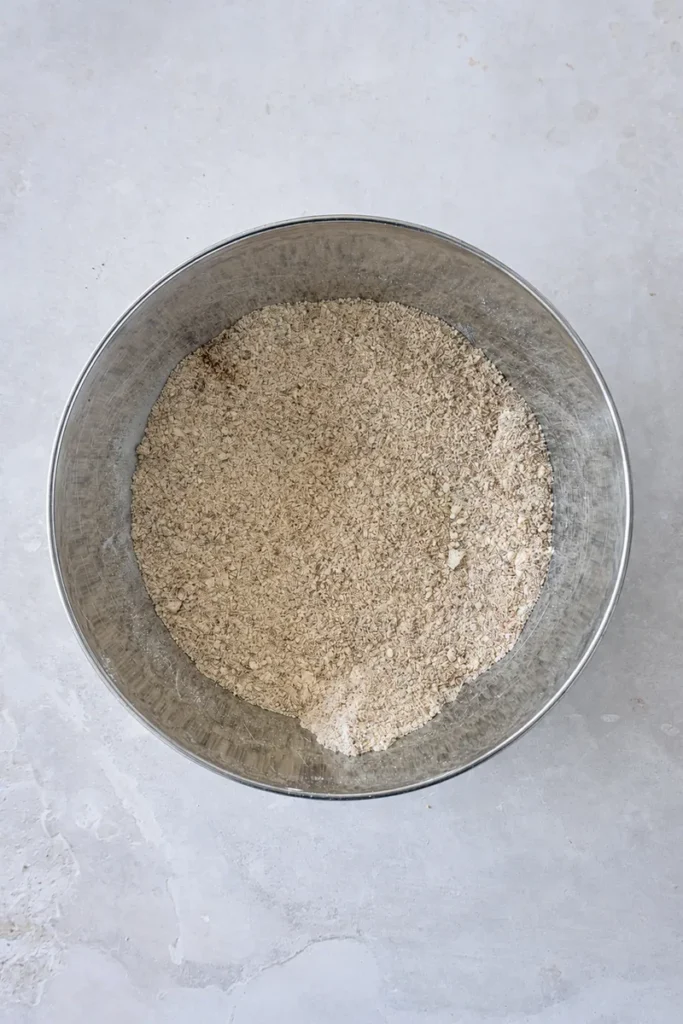 Vegan apple cake dry ingredients mixed in a metal bowl on a pale stone surface.