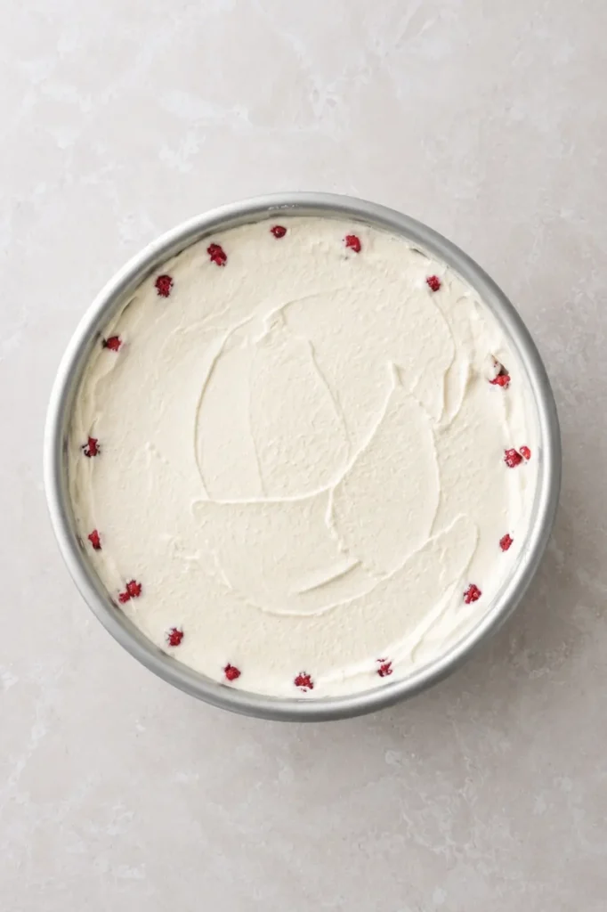 Vegan strawberry cheesecake filling spread over the strawberry-lined crust in a round cake pan.