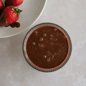 Chocolate sauce with fresh strawberries dipped in glossy chocolate on a neutral countertop.