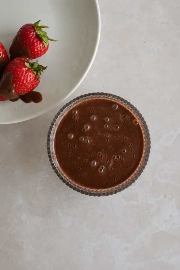 Chocolate sauce with fresh strawberries dipped in glossy chocolate on a neutral countertop.