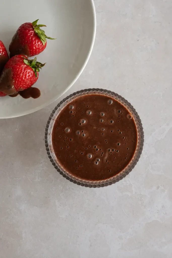 Chocolate sauce with fresh strawberries dipped in glossy chocolate on a neutral countertop.