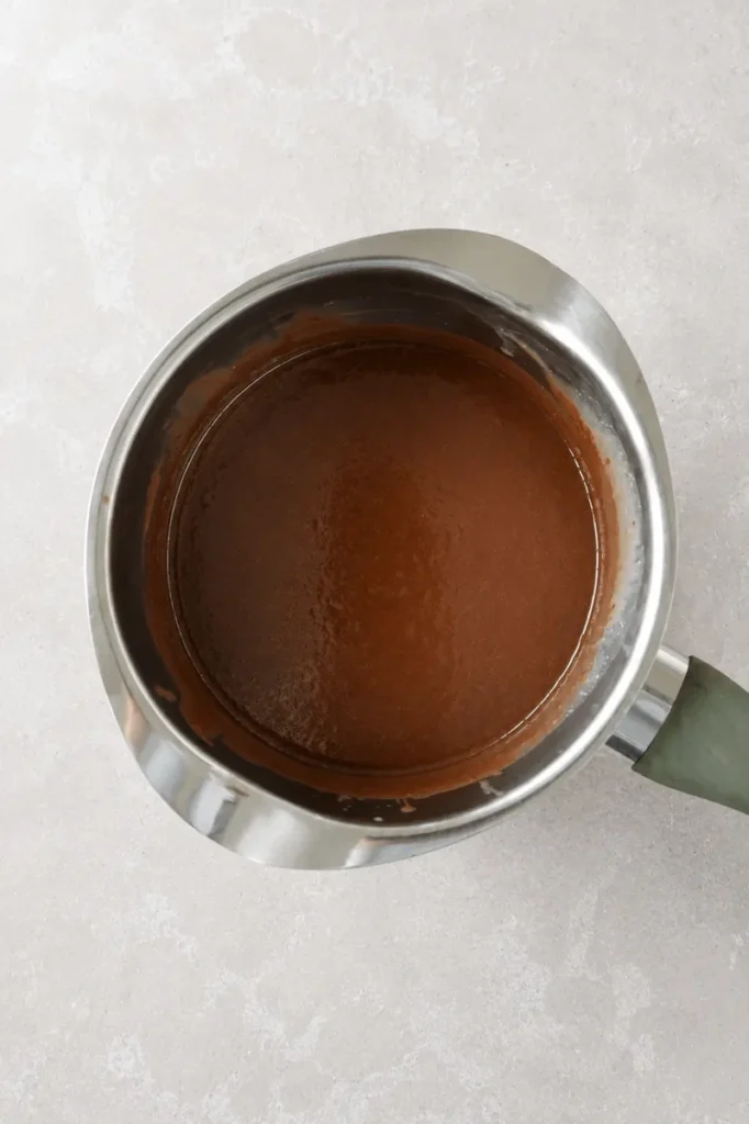 Vegan chocolate sauce cooking in a stainless steel saucepan with a rich, smooth chocolate texture.