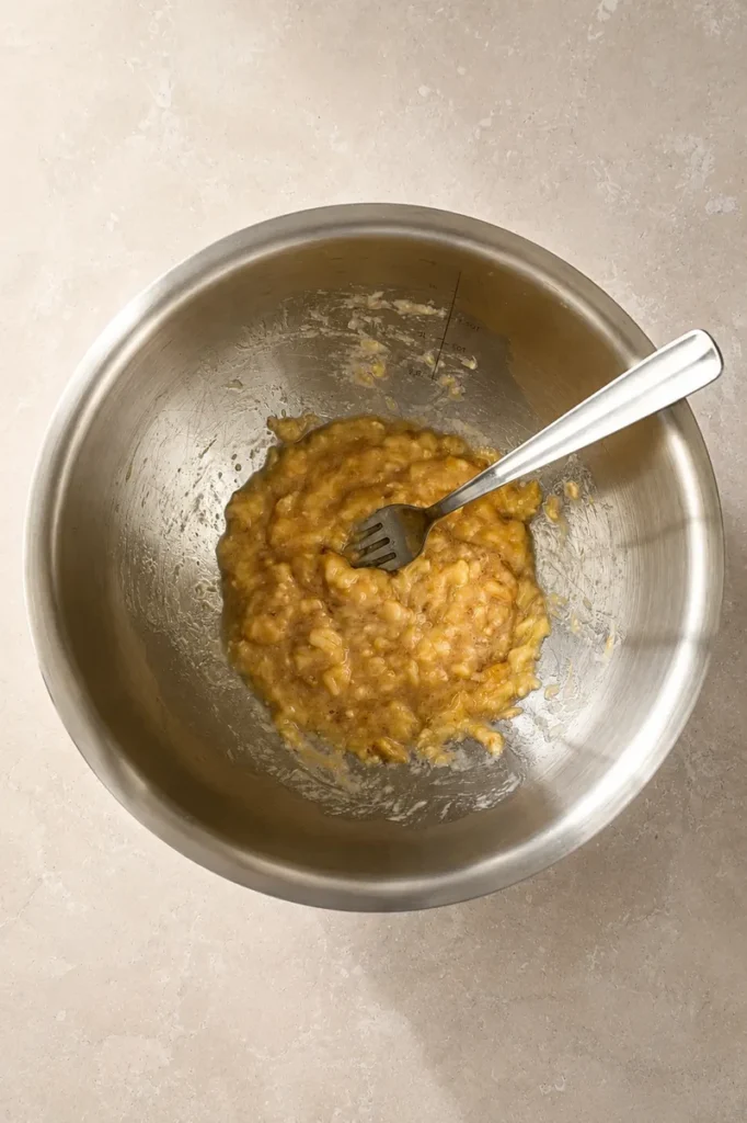 vegan gluten free banana bread mashed bananas in a stainless steel bowl with a fork during recipe preparation.
