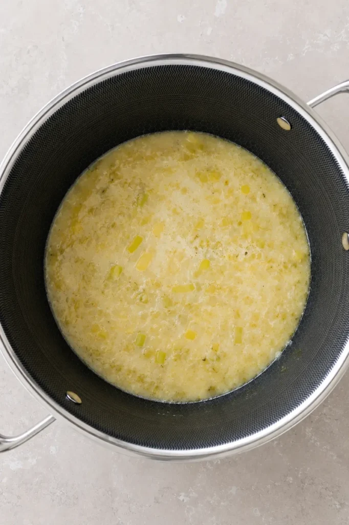 Vegan potato leek soup cooking in a large pot, showing the creamy potato and leek mixture before blending.
