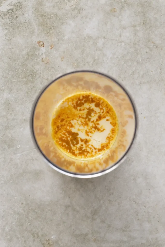 Vegan mayo base in a blender cup with plant milk and turmeric before blending.