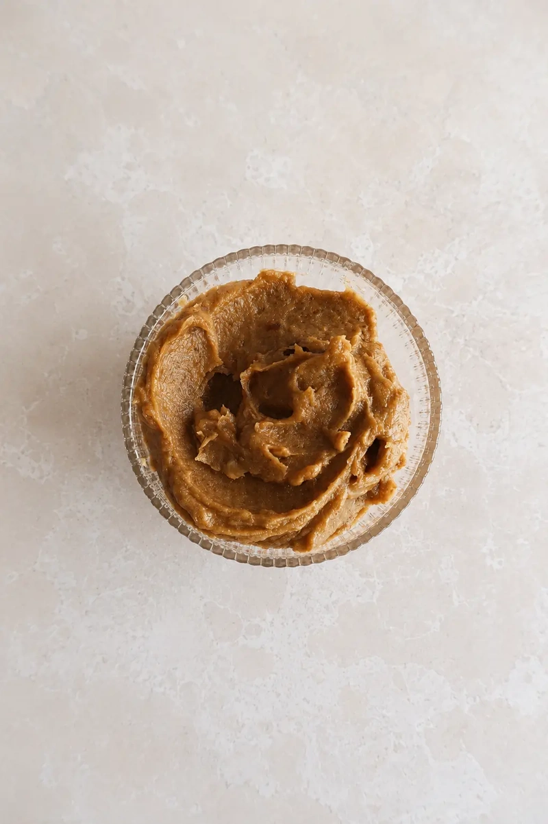 Medjool date caramel sauce in a small glass bowl, photographed from above on a pale stone surface.