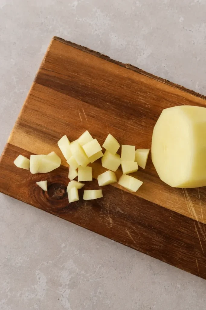 Vegan Split pea soup recipe prep with a peeled potato and diced potato pieces on a rustic wooden board.