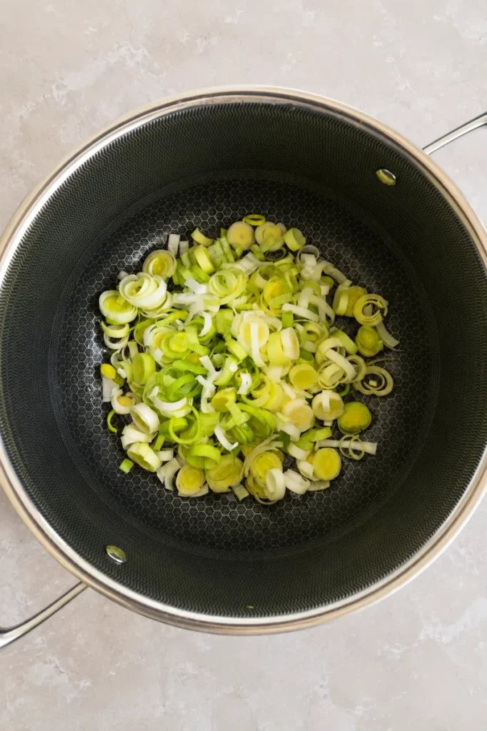 Vegan potato leek soup with sliced leeks added to a large pot before cooking.