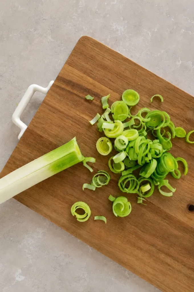 Vegan potato leek soup prep with fresh leek rings sliced on a wooden cutting board.