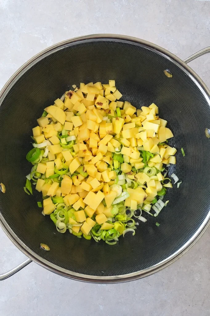 Vegan potato leek soup prep with diced potatoes and sliced leeks in a large pot.