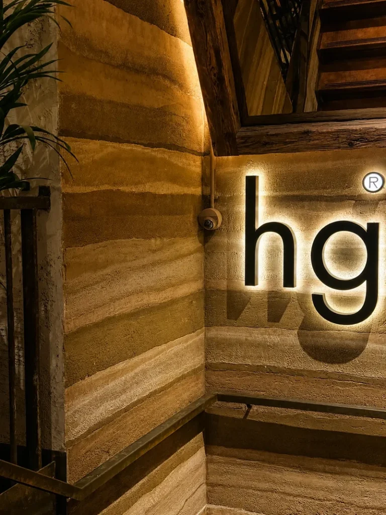 Honest Green London interior with warm lighting, textured earth-toned walls, wooden stairs, and a backlit restaurant sign.