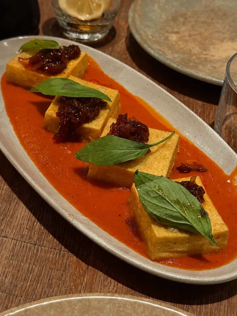 Mallow vegan tofu dish served on a smooth orange cream with fresh herbs and colourful plant-based toppings.