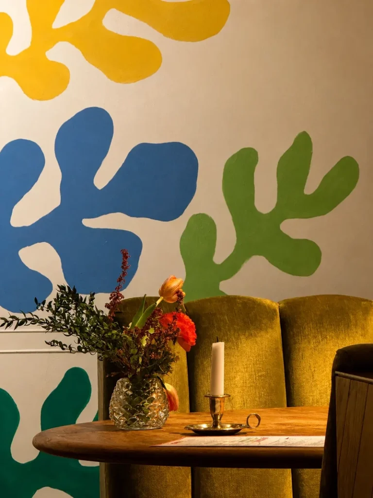 Studio Gauthier London interior with colourful wall art, velvet seating, flowers, and a candle on a wooden table.